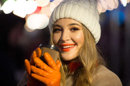 beautiful girl on the background of lights with coffee, on the street, holiday, new year. a walk through the evening city smilesの写真素材