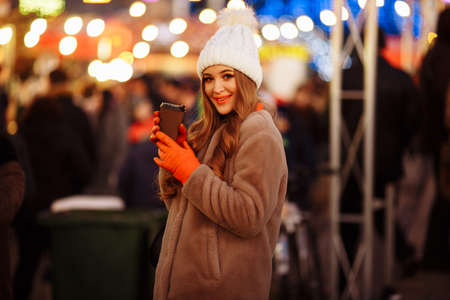 beautiful girl on the background of lights with coffee, on the street, holiday, new year. a walk through the evening city smilesの写真素材