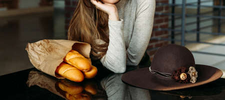 A girl sits around the table on which lies a bread, baguette and brown hat.shopping, cafe, waiting...