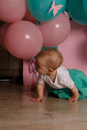 a little girl is sitting on the floor, on a pink background, near the balloons, with a pacifier.celebration. birthday, turned a year old. dress white and blue.Little Girl with soother.の写真素材