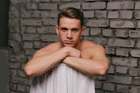 white, attractive man sitting on a chair. portrait, pose, style. background gray wall. white shirt hanging on a chairの写真素材