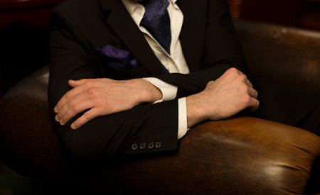 hands of the man lie on the back of the chair, he himself in a dark suit with a purple handkerchief, in a vest sits on a chairの写真素材
