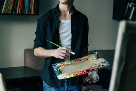 the artist holds a palette with paints and a brush and is going to paint on canvas. a man in jeans and a black shirt. hobby.の写真素材