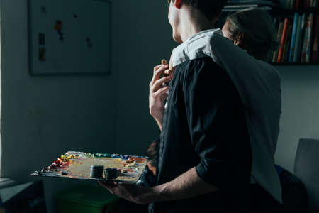 a man holds in his hand a palette with paints and a brush, and behind him they embrace. supportの写真素材