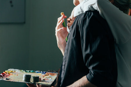 a man holds in his hand a palette with paints and a brush, and behind him they embrace. supportの写真素材