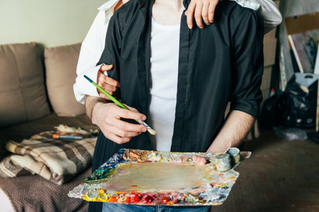 a man holds in his hand a palette with paints and a brush, and behind him they embrace. supportの写真素材