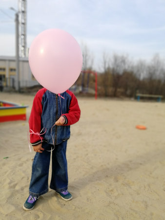 little boy with a balloon pink, instead of head, standing on the street in the sandの写真素材