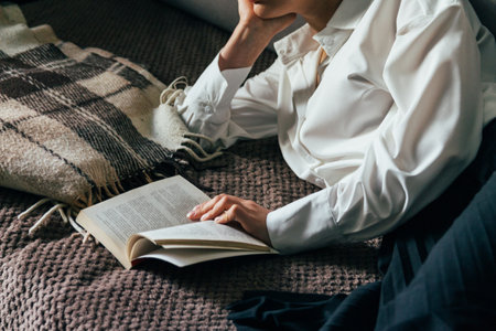 girl reading a book in a warm blanket. woman lies, lay down on the bed, a blanket, a sofa, a couch...