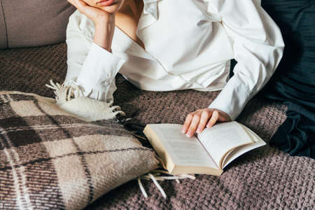 girl reading a book in a warm blanket. woman lies, lay down on the bed, a blanket, a sofa, a couch...