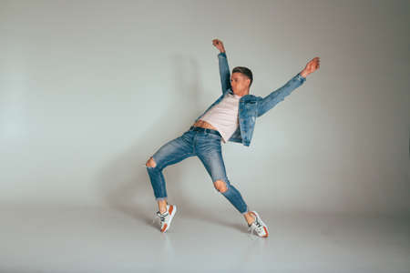 guy dances on a white background in torn jeans, a white tank top and a denim jacket, hands are raised up, jump, pose, styleの写真素材