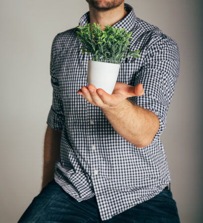 man in a plaid shirt holding a plant in a pot, the concept of taking care of nature, a farmer, growing, harvestingの写真素材