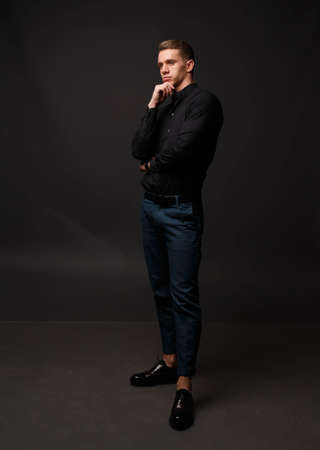 Portrait of a fashionable young man black shirt and blue pants stands on a dark backgroundの写真素材