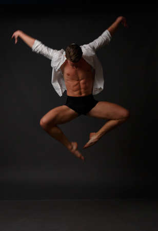 white man in an unbuttoned white shirt and black shorts dancing on a gray background, bare legs and torso, studio shotの写真素材