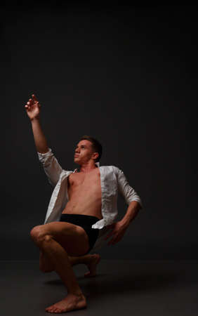 white man in an unbuttoned white shirt and black shorts dancing on a gray background, bare legs and torso, studio shotの写真素材
