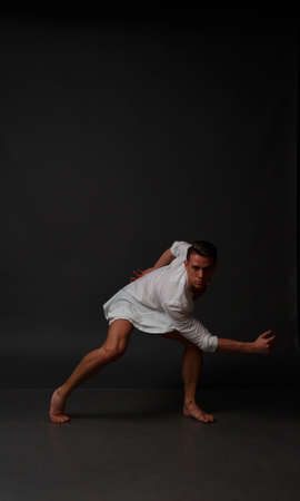 white man in an unbuttoned white shirt and black shorts dancing on a gray background, bare legs and torso, studio shotの写真素材