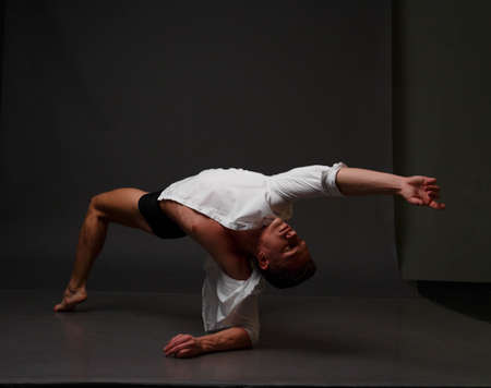 white man in an unbuttoned white shirt and black shorts dancing on a gray background, bare legs and torso, studio shotの写真素材