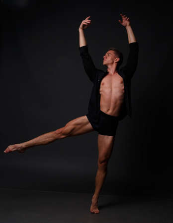 white man in an unbuttoned black shirt and black shorts dancing on a gray background, bare legs and torso, studio shotの写真素材
