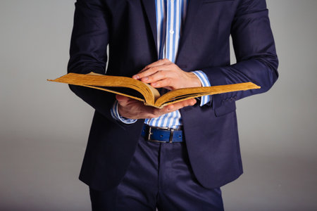a man in a blue suit and a striped shirt is holding an open, old yellow book in his hands, thumbing through pages, readingの写真素材