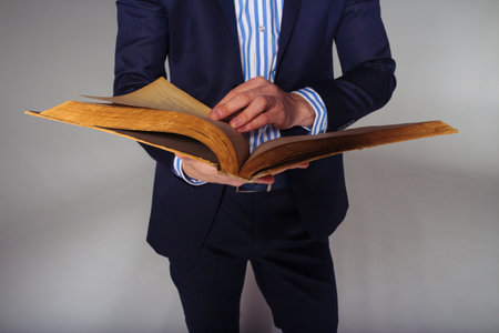 a man in a blue suit and a striped shirt is holding an open, old yellow book in his hands, thumbing through pages, readingの写真素材