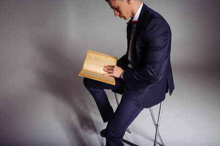 a one man, a guy in a blue suit, sits on a chair and reads an old book, the concept of knowledge, study, science, business, everything new, it's a well-forgotten oldの写真素材