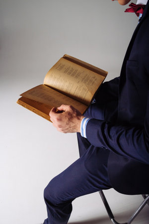 a man in a blue suit sitting on chair, holding an open old yellow book in his hands, thumbing through pages, readingの写真素材