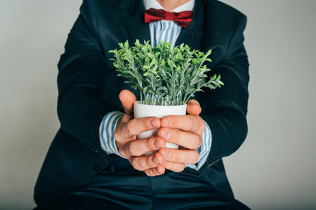 a man in a suit and with a butterfly holding a plant in a white pot, the concept of caring, supporting natureの写真素材