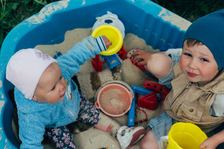 the child is sitting in the sandbox and playing in the sandbox toy balls, shovel, rakes and bucketsの写真素材