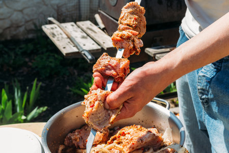a man strings pieces of raw meat on a metal skewer to cook it on fire. Grilled shish kebab. meat on skewers lies on a white tray. barbecue. cook meat with onions and peppers.の写真素材