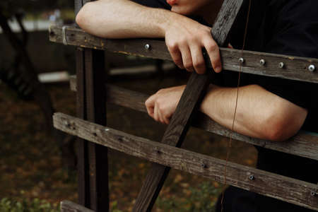 attractive guy on the street, in black, leaning on a hedge, fence