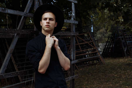 attractive guy in a hat on the street, in black, hat. frowning and straightening his shirt