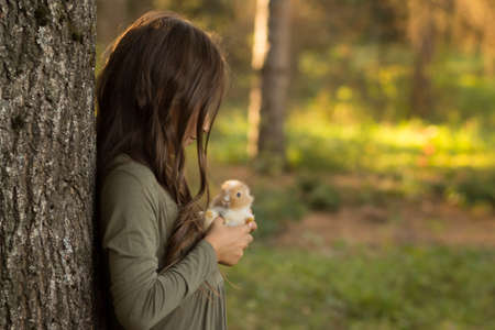 girl with brown hair holds a small, brown with white rabbit in children's hands on a green background, springの写真素材