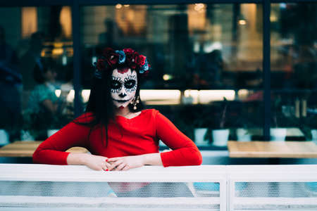 a girl with a painted face of a skeleton, a dead zombie, in the city during the day. day of all...