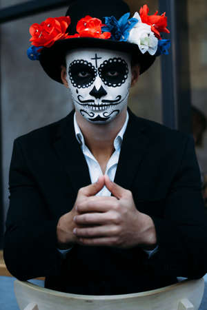 a man with a painted face of a skeleton, a dead zombie, in the city during the day. day of all...