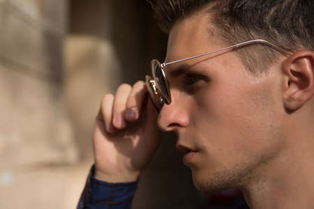 close-up of a man who takes off his sunglasses, male portrait in profile, where he holds glasses,...