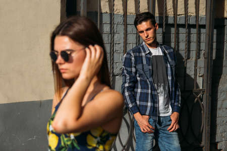 sad guy looks at the trail of the outgoing girl, summer. girl in sunglasses out of focus, from behind a guy near an iron door, lattice.quarrel, resent.go off.girl in sundress, summerの写真素材