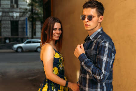 a girl in a sarafan holds a guy's hand in sunglasses. the girl is smiling. the girl has a smart watch on her arm. are going to leave.journey, meetingの写真素材
