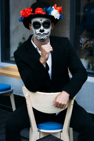 a man with a painted face of a skeleton, a dead zombie, in the city during the day. day of all souls, day of the dead, halloween, ghost walk in a hatの写真素材