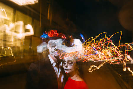 blur of foranium, ghosts of the dead, long exposure. A man and a woman with a visage, a pattern of skulls, a zombie on the face. Dead at night. A pair of zombies in the dark outside, blurry lights, ghosts. The day of the dead and Halloween. long exposure photography, bifurcation.の写真素材