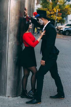 A couple, wearing skull make-up for. All souls day. Boy and girl sugar skull makeup.painted for halloween standing on the street. dead in the city. zombie walk.day of the dead holiday in mexicoの写真素材