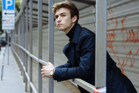portrait of an attractive young man in a blue suit in the city on gray background.watch on hand, gold wrist watch.pensiveの写真素材