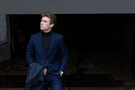 portrait of an attractive young man in a blue suit in the city on gray background.watch on hand, gold wrist watch.pensiveの写真素材