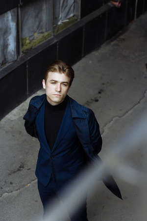 portrait of an attractive young man in a blue suit in the city on gray background.watch on hand, gold wrist watch.pensiveの写真素材