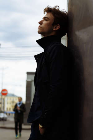 portrait of an attractive young man in a blue suit in the city on gray background.watch on hand, gold wrist watch.pensiveの写真素材