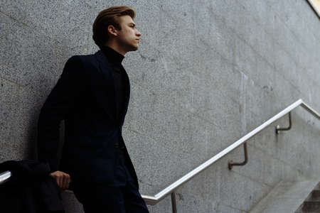 portrait of an attractive young man in a blue suit in the city on gray background.watch on hand, gold wrist watch.pensiveの写真素材