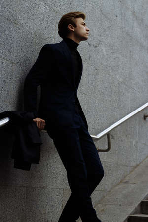 portrait of an attractive young man in a blue suit in the city on gray background.watch on hand, gold wrist watch.pensiveの写真素材