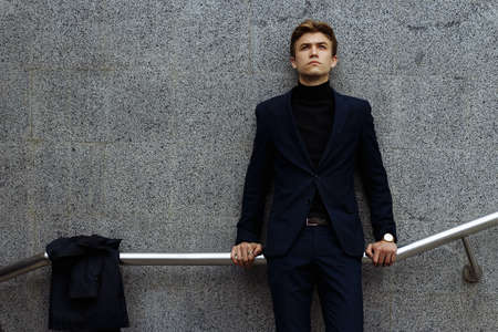 portrait of an attractive young man in a blue suit in the city on gray background.watch on hand,...