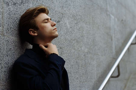 portrait of an attractive young man in a blue suit in the city on gray background.watch on hand, gold wrist watch.pensiveの写真素材