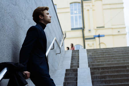 portrait of an attractive young man in a blue suit in the city on gray background.watch on hand, gold wrist watch.pensiveの写真素材