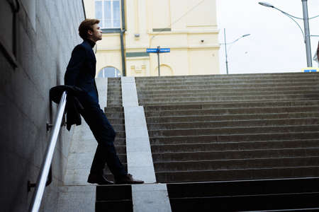 portrait of an attractive young man in a blue suit in the city on gray background.watch on hand, gold wrist watch.pensiveの写真素材