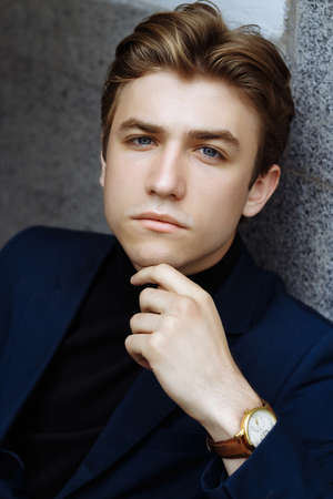 portrait of an attractive young man in a blue suit in the city on gray background.watch on hand, gold wrist watch.pensiveの写真素材